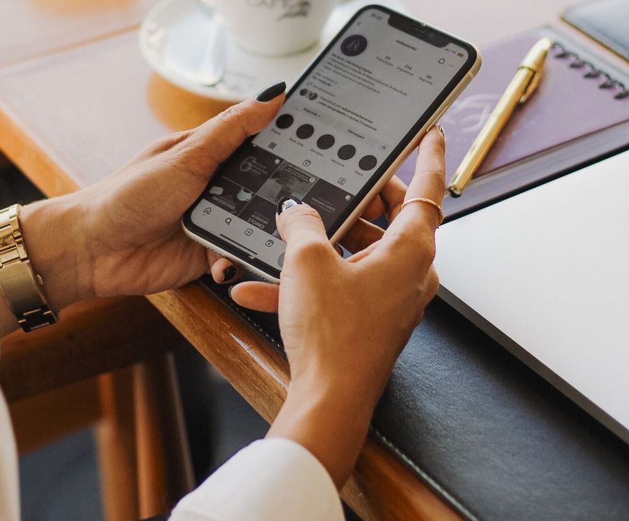Mãos segurando um celular com um perfil de Instagram aberto, em uma mesa de café